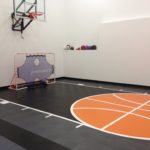 Indoor basketball court by Millz House featuring SnapSports athletic flooring in black and orange