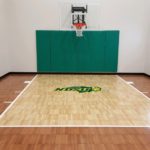 Customized indoor basketball court by Millz House in light and dark maple with custom NDSU logo