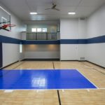 Indoor game court with wall mount basketball hoop and light maple floors with a royal blue basketball key