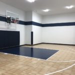 1130 SF Game Court featuring SnapSports athletic tiles in Light Maple Tuffshield with a Navy Revolution Tuffshield lane, white basketball lines, 72" Gladiator basketball hoop, nave wall and corner pads and black cove base
