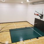 Indoor residential basketball court with maple parquet flooring and green basketball lane
