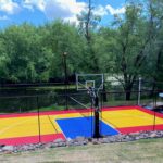 30' × 50' Outdoor Multi-sport Court featuring SnapSports Duracourt Athletic Tiles in Red, Yellow, and Bright Blue, Gladiator 72" Basketball Hoop, White Basketball Game Lines, Black Racket Game Lines, Multi-game Net, Ball Containment, LED Light Pole