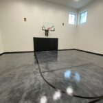 Indoor basketball court featuring metallic floor coating, black game lines, Gladiator 60" adjustable basketball hoop, black wall pad, black cove base