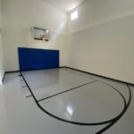 Indoor basketball court featuring floor coating in white knight gray with black game lines, Gladiator 60" fixed basketball hoop, royal blue wall pad and black cove base